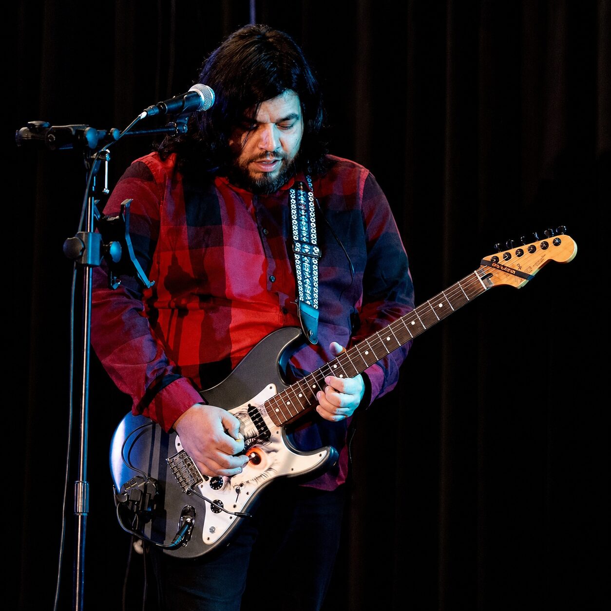 Jesse James Armijo performing on an indoor stage with electric guitar and microphone