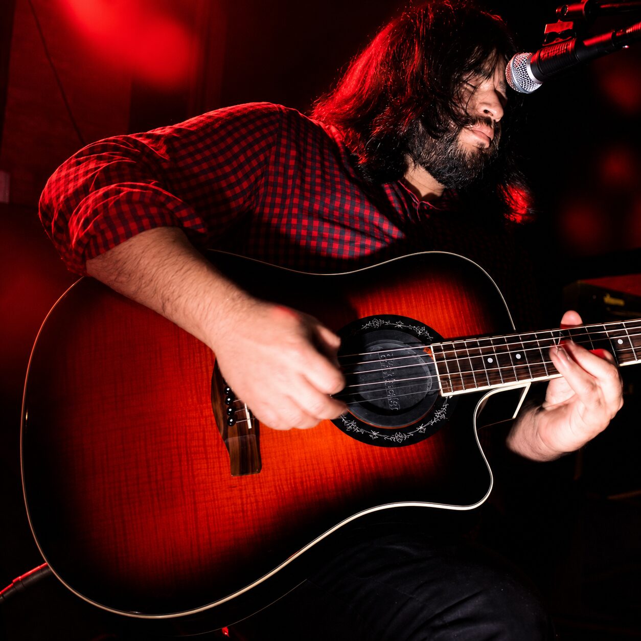 Jesse James Armijo playing electric guitar under red stage lighting